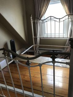 an iron bed frame in front of a window with curtains on the windowsill and wood flooring