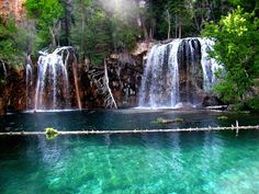 there is a large waterfall in the middle of this lake with clear blue water and green trees surrounding it