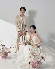 a man and woman sitting next to each other with flowers in front of them on the ground