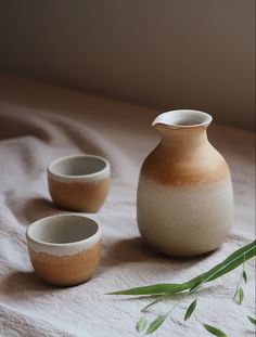 three white and brown vases sitting on top of a bed next to each other