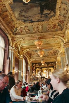 many people are sitting at tables in a large room with paintings on the walls and ceiling