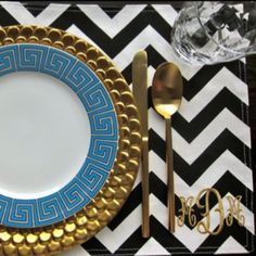 a blue and gold plate sitting on top of a black and white place mat next to silverware