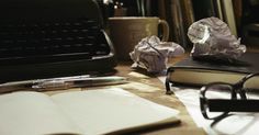 an open book sitting on top of a wooden table next to glasses and a typewriter