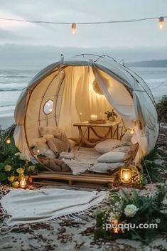 an outdoor tent with lights hanging from the ceiling and pillows on the ground next to it