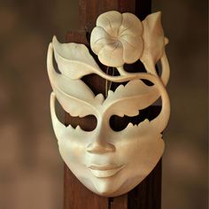 a white mask with flowers on it hanging from a wooden pole in front of a wall