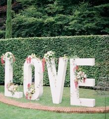 a sign that says love in front of a hedge with flowers and greenery around it