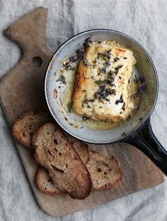 a pan filled with bread and cheese on top of a cutting board next to slices of bread