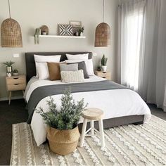 a bedroom with white and grey bedding, plants on the nightstands and hanging baskets