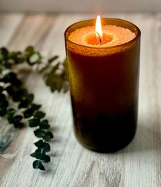 a lit candle sitting on top of a wooden table next to green plants and leaves