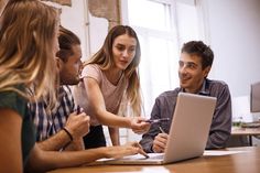 group of people sitting around a table looking at something on the computer screen and laughing