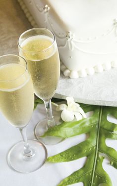 two glasses of champagne next to a wedding cake