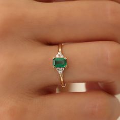 a woman's hand holding an emerald and diamond ring