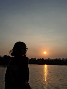 a person standing in front of a body of water with the sun setting behind them