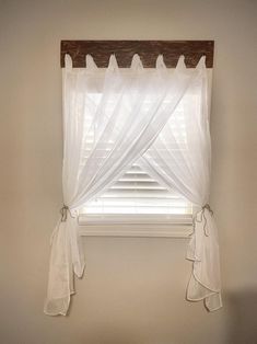 a window with white sheer curtains hanging from it's valance and wooden frame