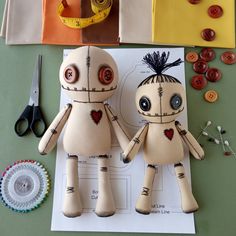 a couple of dolls sitting on top of a piece of paper next to scissors and buttons