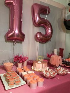 a pink table topped with lots of cupcakes and cake next to giant balloons