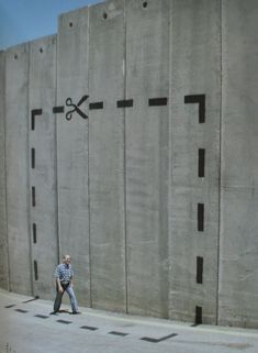 a man walking past a concrete wall with scissors painted on it's side,