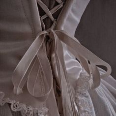 the back of a wedding dress with white lace on it's straps and bows