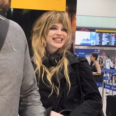 a woman with headphones standing next to a man in a gray shirt and black jacket