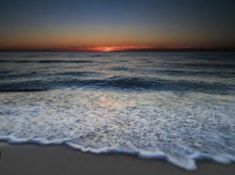 the sun is setting over the ocean with waves coming in to shore and an orange glow on the horizon