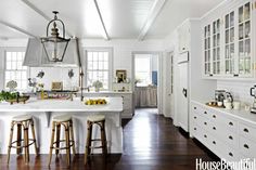 a large kitchen with white cabinets and wooden flooring, along with bar stools