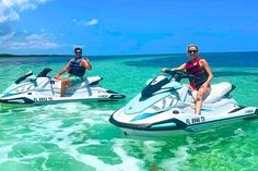 two people riding jet skis in the ocean with clear blue water and bright blue sky