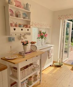 a white kitchen with lots of dishes on the counter and flowers in vases next to it