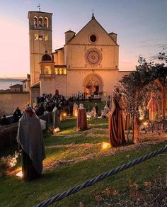 a group of people standing in front of a church with candles on the ground and trees