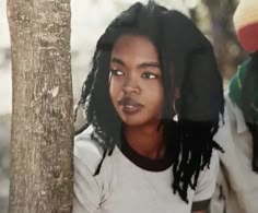 a woman with dreadlocks standing next to a tree in front of a man