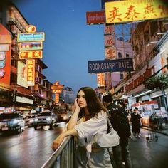 a woman leaning on a railing in the middle of a busy city street at night