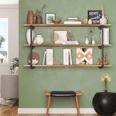 a room with green walls and shelves filled with books, vases and other items