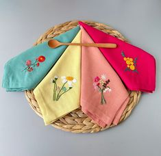 four napkins with embroidered flowers on them and a wooden spoon sitting in the middle