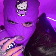 a woman wearing a purple hello kitty hat and holding a drink in her hand while covering her face