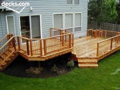 a wooden deck with stairs and railings in front of a house on the grass