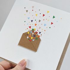 a hand holding a brown envelope with confetti and hearts coming out of it