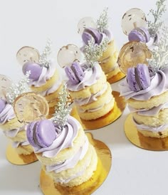 small cupcakes are decorated with purple icing and silver decorations on gold plates