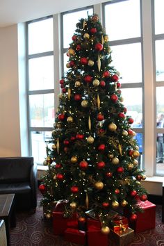 a christmas tree with presents under it in front of a large window at an airport