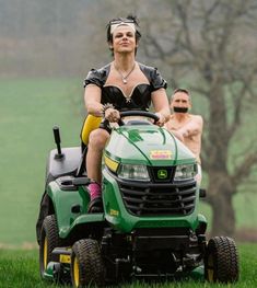 a woman riding on the back of a green lawn mower next to a man