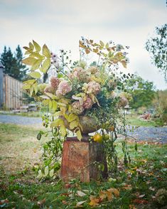 a vase filled with lots of flowers sitting on top of a wooden stump in the grass