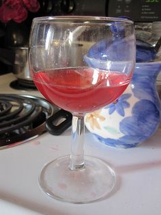 a glass of red wine sitting on top of a counter next to a pot and pan