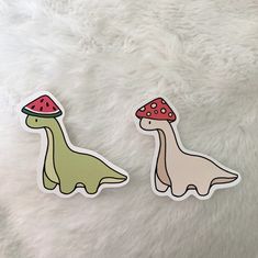 two stickers depicting dinosaurs with mushrooms on their heads, one is green and the other is pink