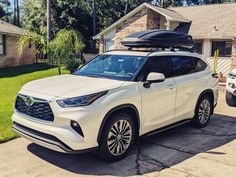 a white suv parked in front of a house with a surfboard on the roof