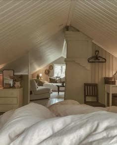 an attic bedroom with white bedding and furniture