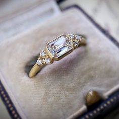 an engagement ring with three stones in it sitting on a cushioned velvet box,