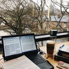 an open laptop computer sitting on top of a wooden desk next to a cup of coffee