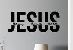 the word jesus is written in black on a wall next to a vase and lamp