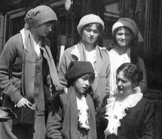 an old black and white photo of four women standing next to each other in front of a train