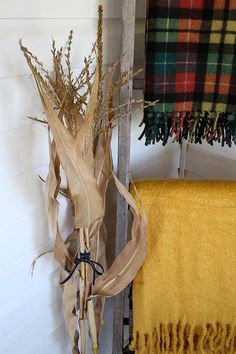 an old ladder with some dried plants in it and a plaid blanket hanging on the wall