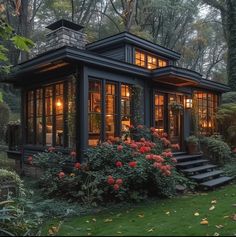 a small house with lots of windows and flowers in the front yard, surrounded by trees