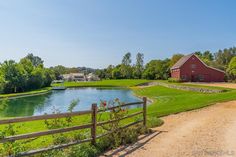 a red barn sitting next to a lake in the middle of a lush green field